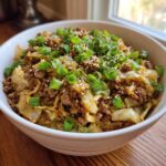 A close-up of a white bowl filled with savory egg roll in a bowl mixture, topped generously with chopped green onions and sesame seeds.