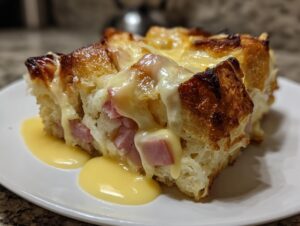 A close-up of a serving of eggs benedict casserole with ham, topped with melted cheese and hollandaise sauce.