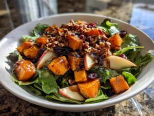 Close-up of a vibrant fall harvest salad featuring roasted orange squash, apple slices, pecans, and dried cranberries over greens.