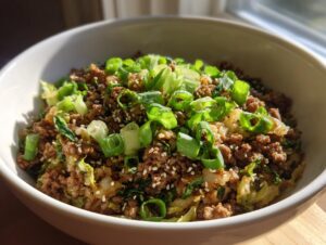 Close-up of a white bowl filled with savory egg roll in a bowl mixture, topped with sesame seeds and fresh green onions.