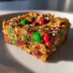 A single square of chewy christmas cookie bars topped with red and green M&Ms and holiday sprinkles.