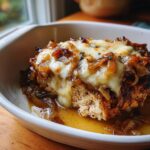 Close-up of a serving of french onion chicken topped with melted cheese and caramelized onions in a white dish.