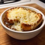 Close-up of a bowl of french onion soup recipe topped with a thick, toasted crouton covered in gooey, melted Gruyère cheese.