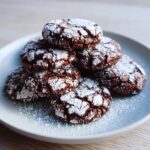 A stack of rich, dark chocolate crinkle cookies heavily dusted with white powdered sugar.