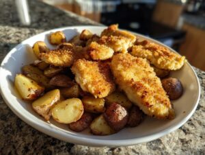 Golden brown, breaded garlic parmesan chicken tenders served over roasted potatoes in a white bowl.