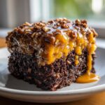 Close-up of a square slice of rich, dark german chocolate poke cake topped with gooey caramel frosting and chopped pecans.