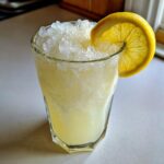 A tall glass filled with homemade lemonade and crushed ice, garnished with a fresh lemon slice.