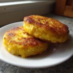 Two perfectly golden brown, round fried cornbread patties stacked slightly on a white plate.
