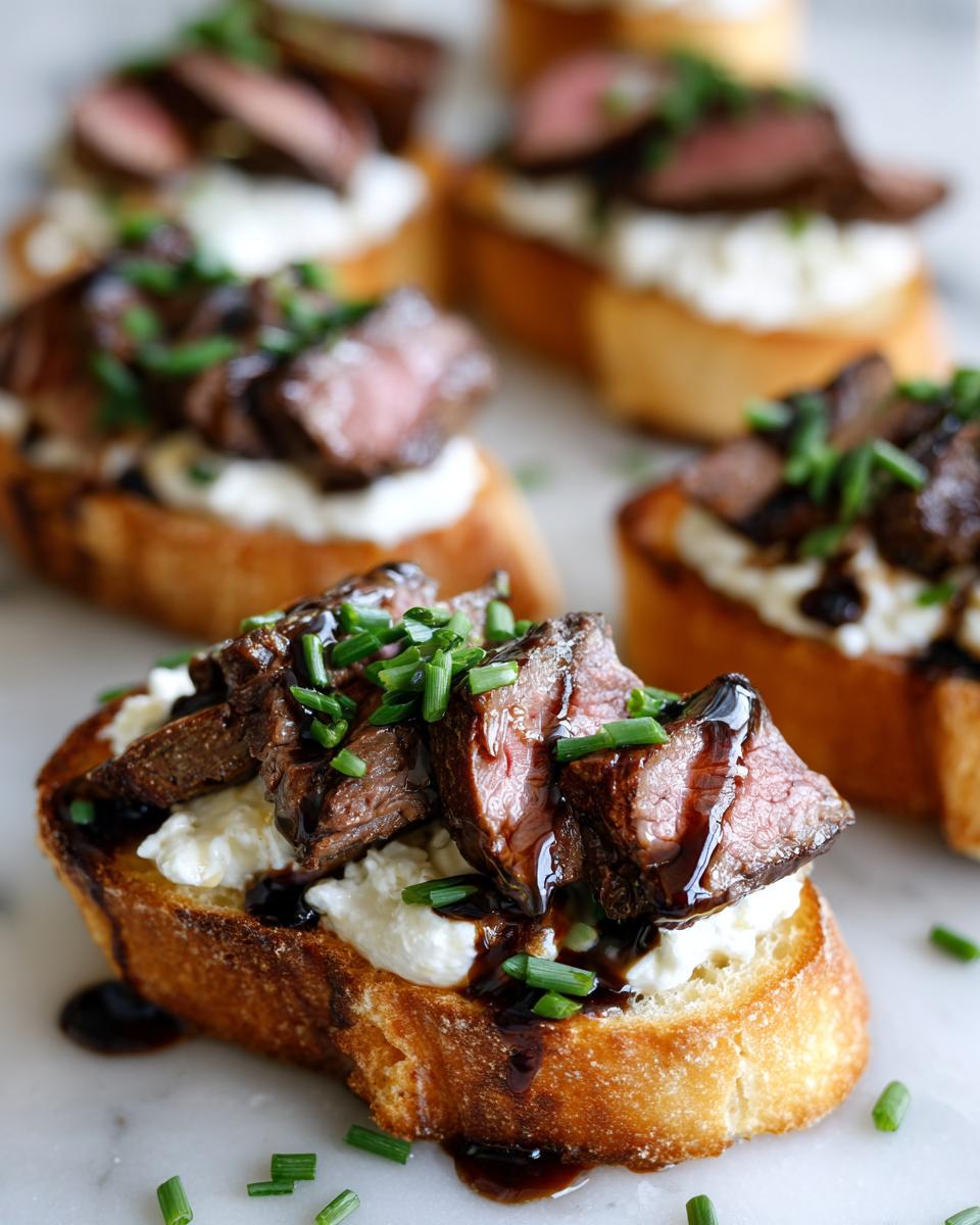 Close-up of a perfectly prepared steak crostini topped with creamy cheese, sliced medium-rare steak, and fresh chives.