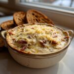 A hot, baked reuben dip topped with melted and shredded cheese, served with slices of dark rye bread.