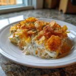 A generous serving of hot chicken salad casserole topped with golden, crunchy cornflakes on a white plate.