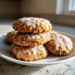 A stack of four soft, round iced oatmeal cookies with a white glaze drizzled on top.