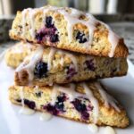 Three stacked lemon blueberry scones, generously filled with blueberries and drizzled with a thick white glaze.