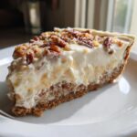 Close-up of a creamy slice of million dollar pie with a graham cracker crust topped with pecans.