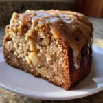 Close-up of a moist slice of apple dapple cake topped with a thick caramel sauce dripping down the side.