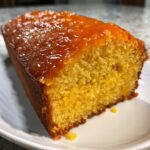 Close-up of a moist slice of bright yellow orange juice cake topped with a shiny, thick orange glaze.