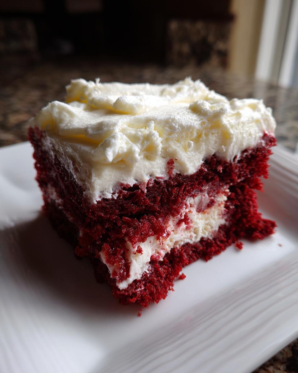 Close-up of a moist slice of red velvet poke cake topped with thick cream cheese frosting.