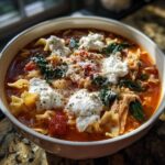 Close-up of a hearty bowl of one pot lasagna soup topped with dollops of ricotta, grated Parmesan, and herbs.
