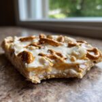 A close-up, low-angle shot of a thick slice of peanut butter pretzel bark topped with white chocolate and small pretzel pieces.