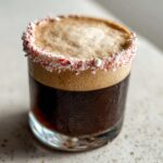 Close-up of a peppermint espresso martini with a thick layer of foam and a rim coated in crushed candy canes.
