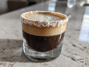 A close-up of a peppermint espresso martini in a rocks glass with a crushed candy cane rim.