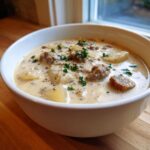 A close-up of a bowl of creamy potato and sausage chowder, garnished with fresh parsley.