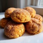 A close-up stack of soft, round pumpkin snickerdoodle cookies generously coated in cinnamon sugar.