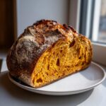 Cross-section view showing the vibrant orange crumb of a freshly baked pumpkin sourdough loaf on a white plate.
