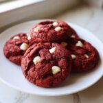 A stack of four rich, deep red velvet cake mix cookies studded with white chocolate chips on a white plate.