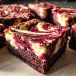 A close-up of a rich, fudgy square of red velvet cheesecake brownies showing the distinct red and cream cheese swirl.