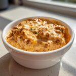 Close-up of a warm, creamy sausage cream cheese dip served in a white bowl, garnished with herbs.