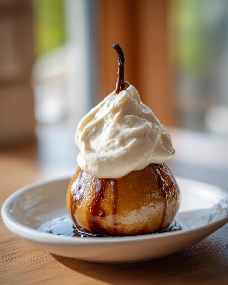 A single, glossy poached pear topped with a dollop of whipped cream and drizzled with syrup.