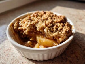 Close-up of a warm, freshly baked apple crumble in a white ramekin with a golden, crunchy topping.