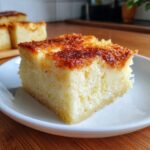 A square slice of moist, creamy cassava cake with a deeply caramelized, golden-brown top, served on a white plate.