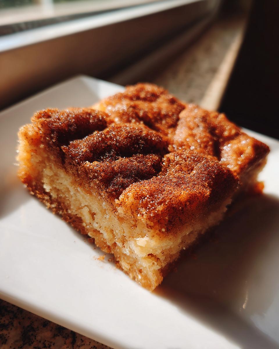 A close-up, sunlit shot of a single square of snickerdoodle blondies topped with cinnamon sugar.