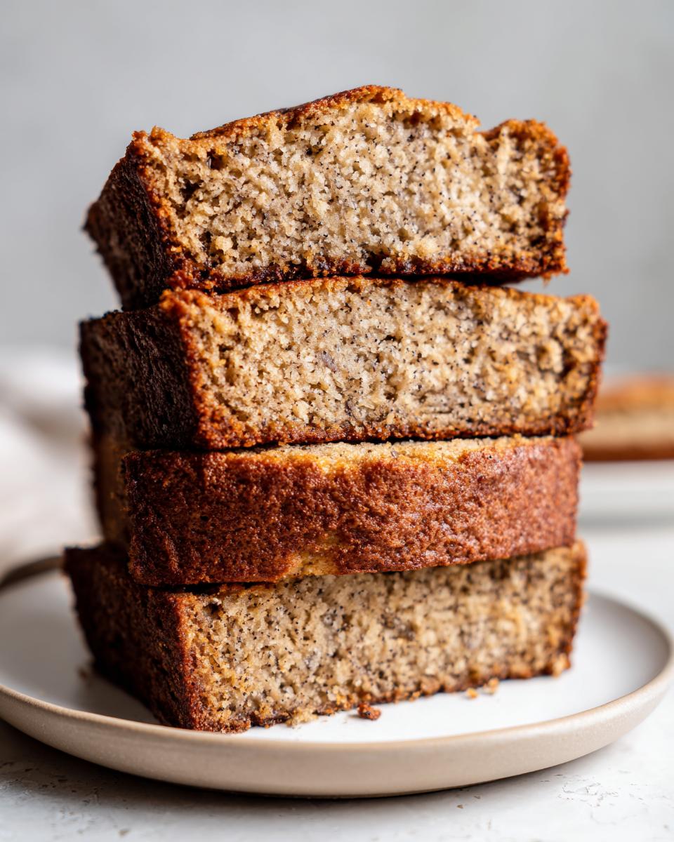 Four thick slices of moist sourdough banana bread stacked on a small plate, showing the speckled crumb.