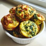 A stack of golden brown spinach egg bites piled high in a small white bowl.