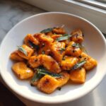A bowl of pan-seared sweet potato gnocchi tossed in brown butter and topped with fresh sage leaves.