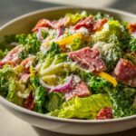 A close-up, vibrant image of a fresh grinder salad featuring romaine lettuce, salami, red onion, yellow peppers, and grated cheese.