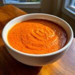 A close-up of a bowl filled with ultra creamy tomato bisque, showing a rich orange-red color and swirl marks.