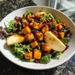 Close-up of a vibrant fall harvest salad featuring roasted butternut squash cubes, apple slices, pecans, and dried cranberries over mixed greens.