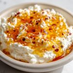 Close-up of a creamy whipped ricotta dip drizzled with golden honey, sesame seeds, and red chili flakes.