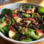 Close-up view of a vibrant apple salad featuring crisp greens, diced red apples, candied pecans, and dried cranberries tossed in a vinaigrette.