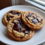 Close-up of three perfectly baked chocolate chip cookie rounds with melted centers and flaky sea salt.