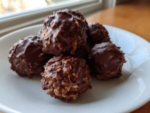 A close-up of several amazing chocolate rice krispie balls coated in rich, textured chocolate, resting on a white plate.