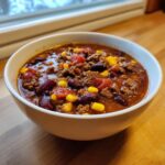 Close-up of a white bowl filled with rich, hearty cowboy soup featuring ground beef, kidney beans, corn, and tomatoes.