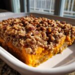 Close-up of a rich, orange slice of sweet potato casserole topped with a crunchy pecan streusel topping.