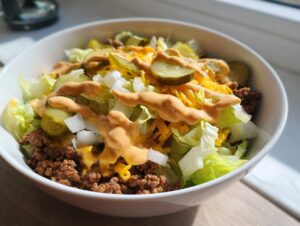 A close-up view of a Big Mac Salad featuring ground beef, lettuce, cheese, pickles, and special sauce in a white bowl.