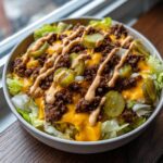 A close-up of a Big Mac Salad featuring lettuce, seasoned ground beef, melted cheese, pickles, and special sauce drizzle.