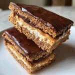 Two stacked bars of buckeye graham crackers dessert showing graham cracker layers, peanut butter, marshmallow, and chocolate topping.